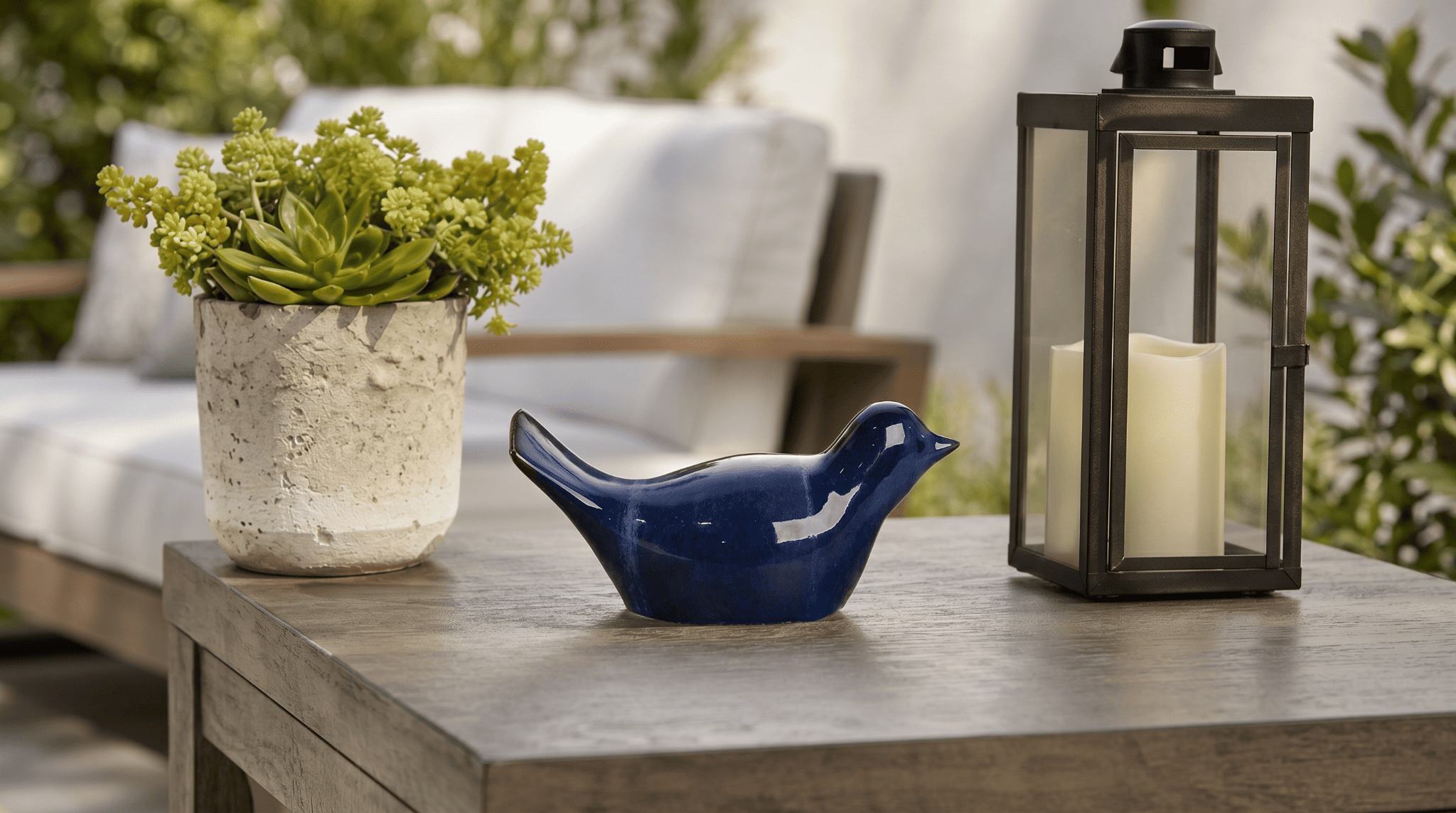 Hattongate blue reactive-glaze ceramic bird garden statue on a patio table beside a succulent and lantern